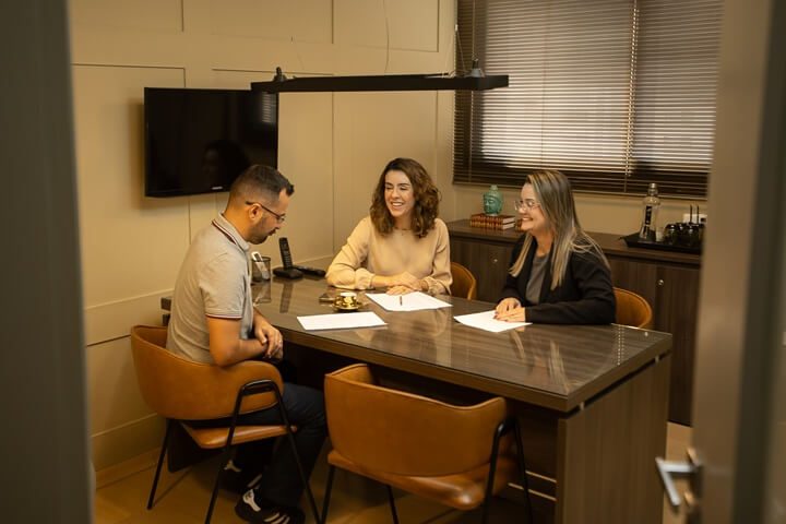 Atendimento ao cliente em sala de reunião por hora em Goiânia — três pessoas em conversa com documentos sobre a mesa, Setor Marista